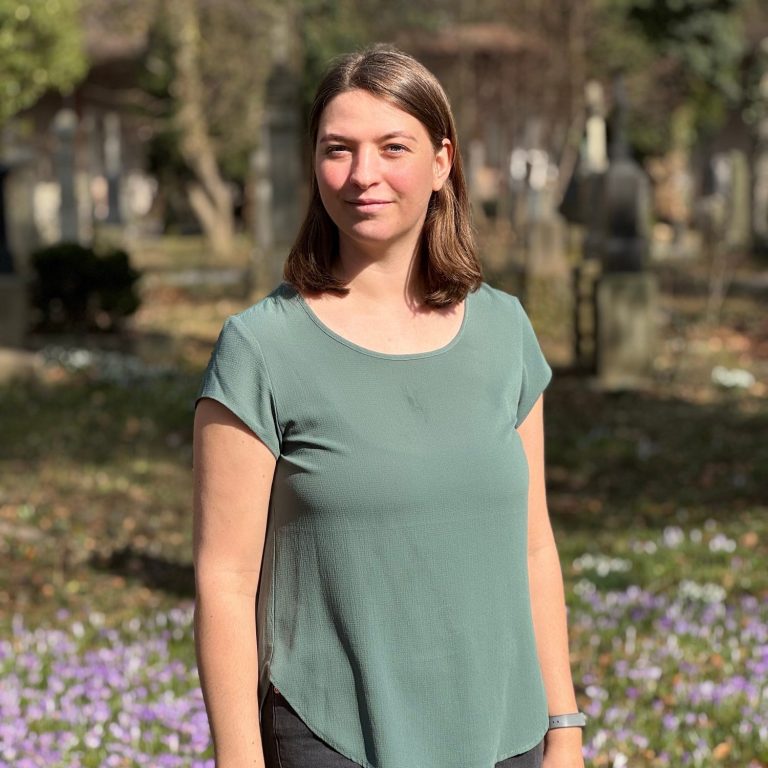 Psychotherapeutin Hanna Baumeister Frau mit braunen Haaren steht in einem Park, umgeben von Blumen und Bäumen.